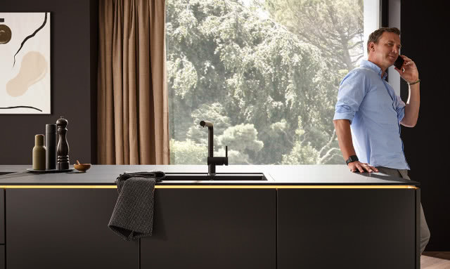 czarne fronty kuchenne, wyspa kuchenna, Mężczyzna rozmawiający przez telefon, zasłony, duże okno, obraz