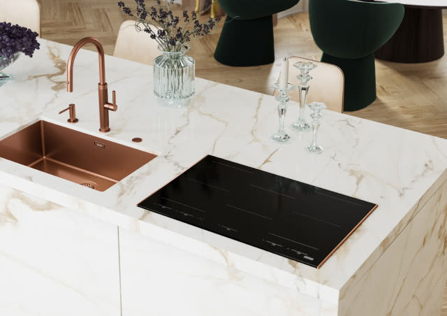 Płyta indukcyjna Mythos Masteriece z detalem w kolorze miedzianym, który pasuje do pozostałych urządzeń na wyspie kuchennej