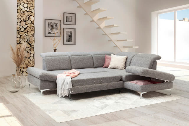 szara kanapa, dwa kwadratowe czarne stoliki kawowe, drewniane schody, drewno do kominka, wazony, obrazy, biały dywan, białe i różowe poduszki ozdobne, koc