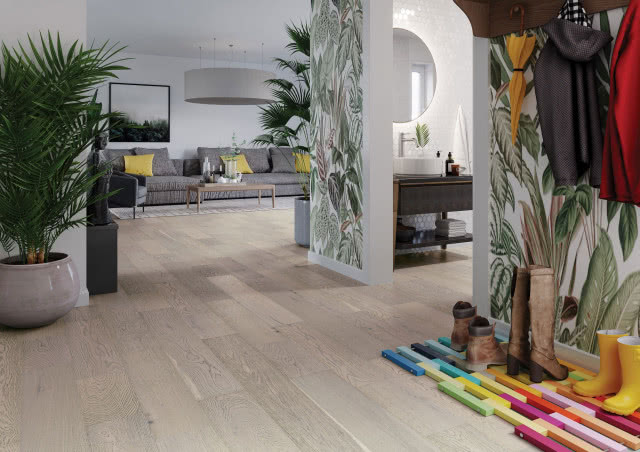 duże palmy, drewniana podłoga, szara kanapa, tapeta z motywem roślinnym, stolik kawowy, rzeźba, parasolka, kurtki, wieszak na ubrania, buty, szafka umywalkowa, umywalka nablatowa, okrągłe lustro łazienkowe