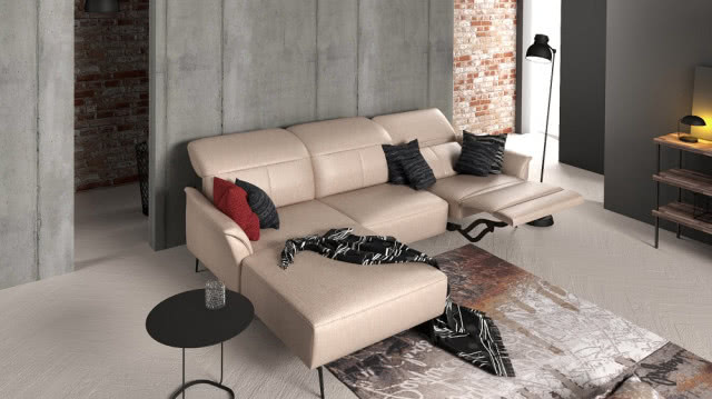 beżowa kanapa, poduszki ozdobne w kolorze czarnym i czerwonym, czarny okrągły stolik kawowy, dywan, lampa podłogowa, beton i cegła na ścianach, lampa biurkowa