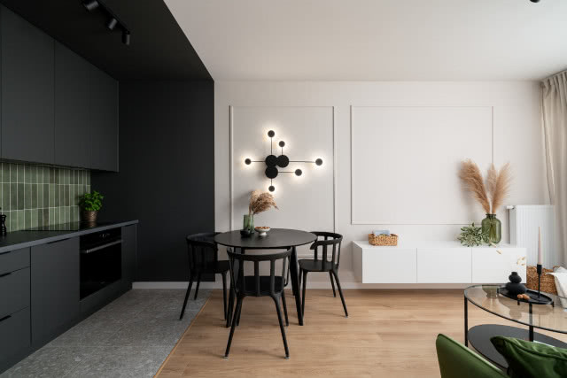 Czarna kuchnia i jasne ściany w salonie ze sztukaterią