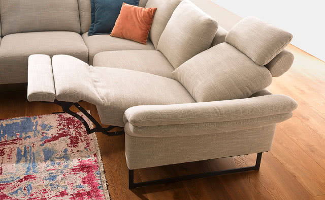 beżowa kanapa z wysuniętą podpórką pod nogi, drewniana podłoga, dywan poduszki ozdobne