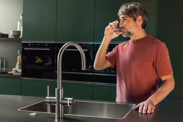 Mężczyzna pije wodę bezpośrednio z nowoczesnej baterii kuchennej Franke Mythos Water Hub, oferującej wodę filtrowaną prosto z kranu