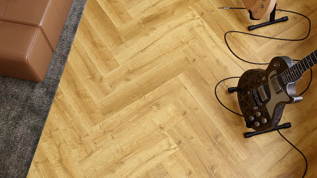 Panele winylowe VIN IN w dekorze dębu ułożone w jodełkę, z gitarą elektryczną na pierwszym planie.