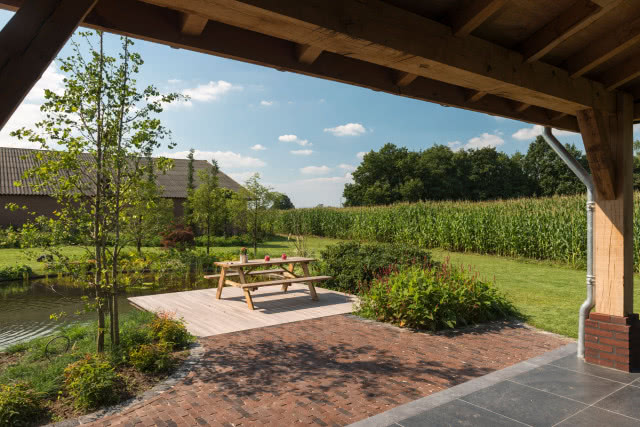 kostka brukowa na tarasie i w ogrodzie, drewniany stół z ławkami, oczko wodne, drzewa, trawa, kwiaty, kukurydza
