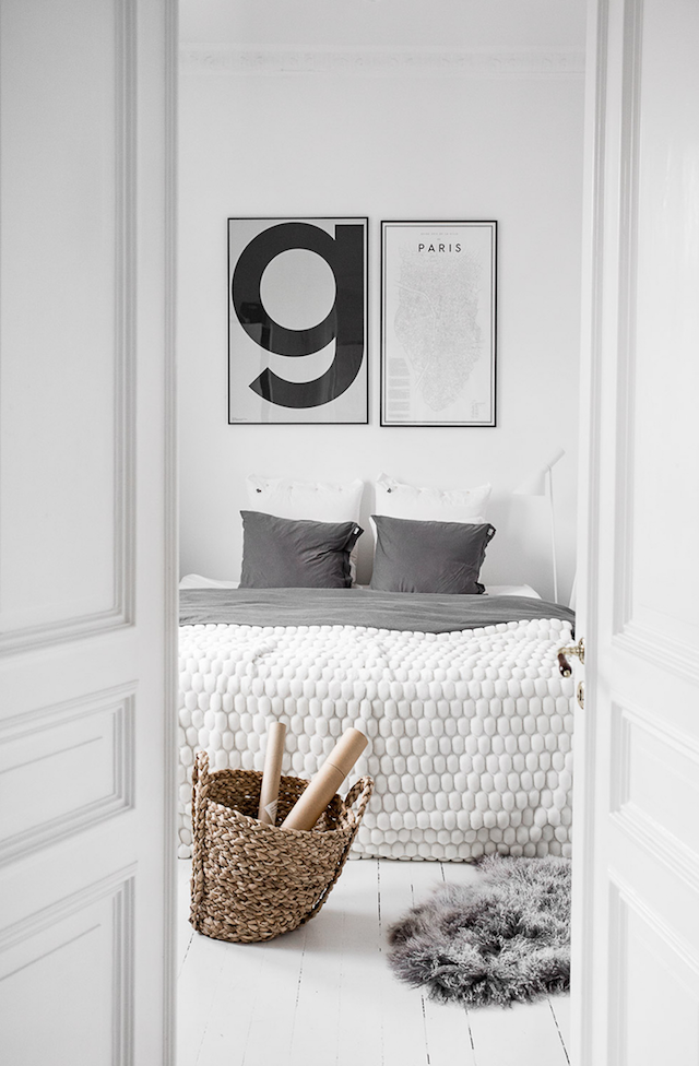 Sypialnia z białymi ścianami i plakatem nad łóżkiem pościelonym kocem z wełny czesankowej