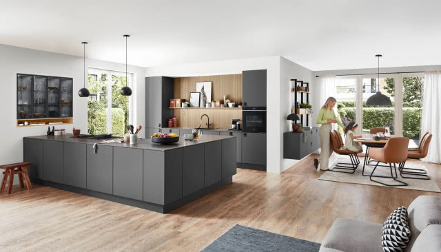wyspa kuchenna w kształcie litery L, szare fronty kuchenne, duży stół z krzesłami, kanapa