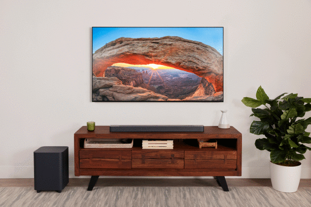 JBL Bar 500, półki, komoda, duży telewizor, kwiaty w doniczce, kanapa, dywan, duży głośnik, lampa podłogowa