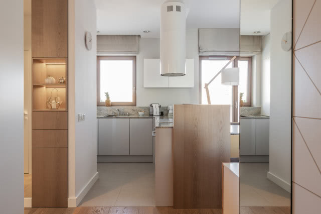 Szafki kuchenne wtapiają się w całość aranżacji. Otrzymały fronty z lakierowanej płyty mdf w kolorze szarym, blat wykonany został z granitu. Minimalistyczny okap Cylindra Isola pochodzi z oferty marki Faber.