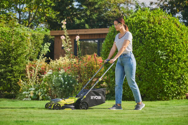 Uśmiechnięta kobieta przycina trawnik przy pomocy kosiarki RYOBI
