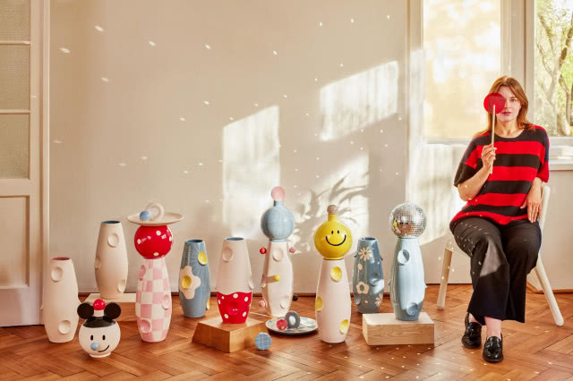 kobieta obok kolekcji zabawnych wazonów w kwiaty, muchomory, buźki, etc.