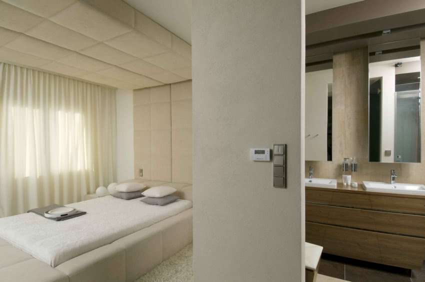 Beżowa przytulna sypialnia sąsiaduje z łazienką.