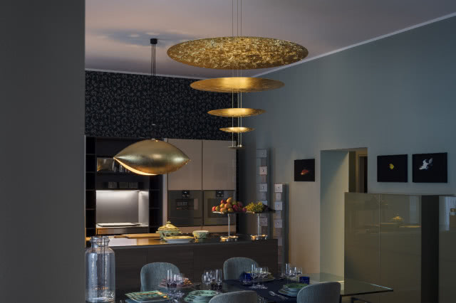 Dzięki zastosowaniu dwóch złotych lamp marki Catellani & Smith - nad stołem piętrowa Macchina della Luce, a nad wyspą kuchenną przypominająca UFO Malagola - całe wnętrze tonie w miękkich i miłych dla oczu bursztynowych tonach