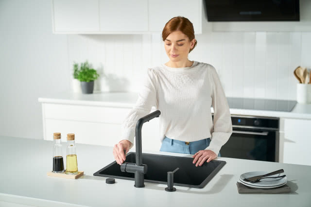 białe meble kuchenne, zioła, płyta indukcyjna, czarna bateria zlewozmywakowa, czarny zlewozmywak, talerze, sztućce
