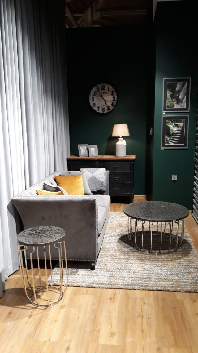 Nowy salon Dekorii w Warszawie! zbutelkowa zieleń na ścianach, okrągły stolik kawowy, szara sofa, żółte poduszki biała lampa
