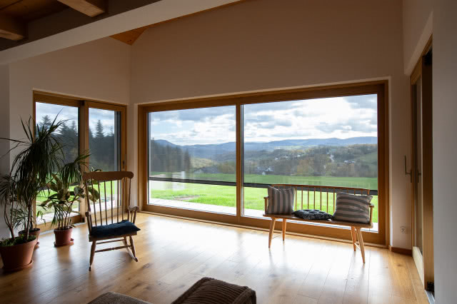 salon, duże okna, krzesło na biegunach, kwiaty w doniczkach, drewniana podłoga, ławka, ozdobne poduszki, belki na suficie