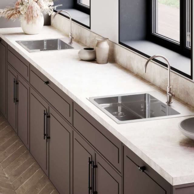 dwa zlewy, srebrne baterie zlewozmywakowe, ciemne fronty kuchenne, blat ze spieku, okna, jodełka na podłodze, wazon z kwiatami