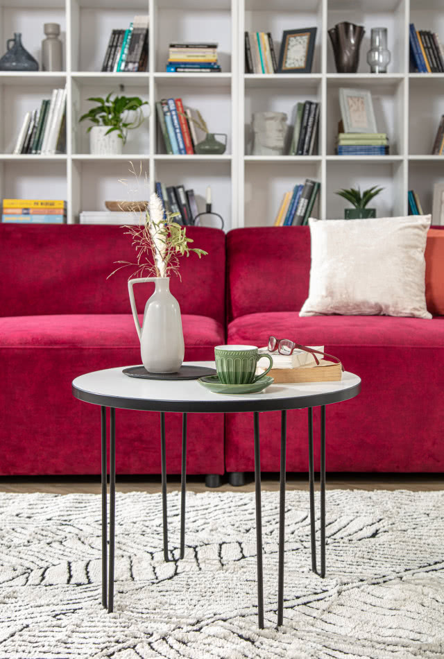 czerwona kanapa, stolik kawowy, półki na książki, wazon, filiżanka, poduszka ozdobna, dywan