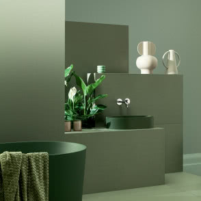 łazienka w kolorze zielonym, zielona wanna wolnostojąca, srebrna bateria wannowa, zielona umywalka nablatowa, stołek, pufa, kosmetyku, ręcznik