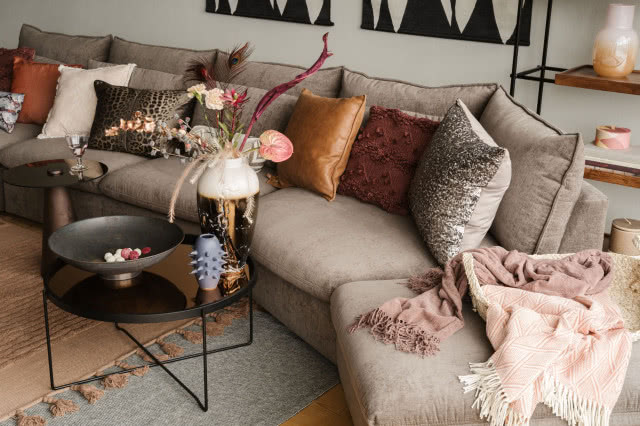 sofa modułowa zaokrąglona, poduszki ozdobne, stolik kawowy, misa, wazony, obrazy, koce, półki, świece, dywan