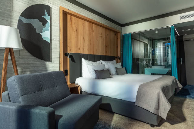 kadr na łóżko w pokoju, w głębi przeszklona łazienka