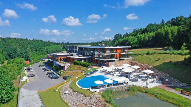 widok na hotel, przed nim basen i parking