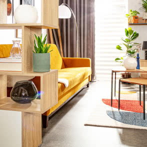 żólta wersalka, fotele, duże lustro, stołek, stoliki kawowe, komoda, półki kwiaty, lampa podłogowa