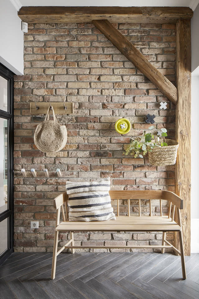 Ściana z cegły w przedpokoju na tle drewnianej ławki