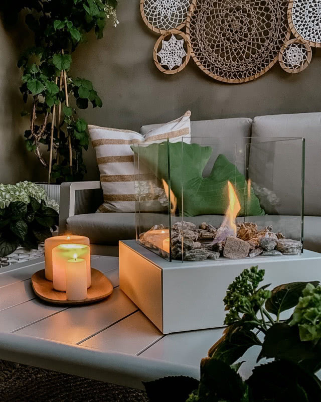 makrama, biokominek wolnostojący, stolik, świece, kanapa, duży zielony kwiat