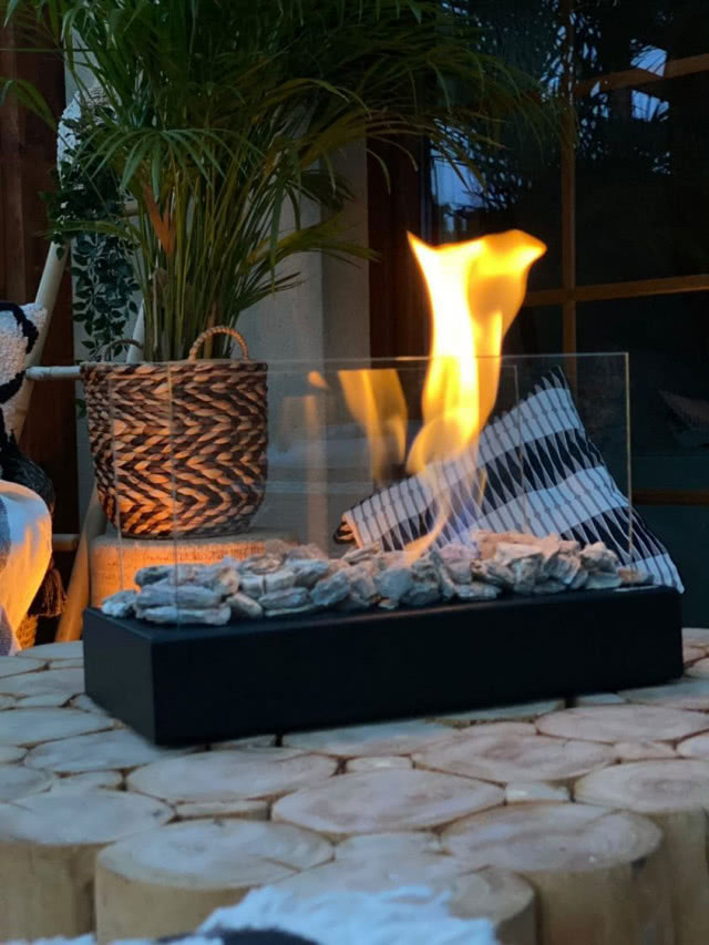 biokominek wolnostojący, stół, duży zielony kwiat w doniczce, duże okno, płomień