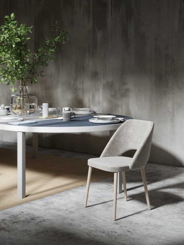 drewniane krzesło obite materiałem, dywan, duży okrągły stół zastawa stołowa, wazon z kwiatami, beton na ścianie