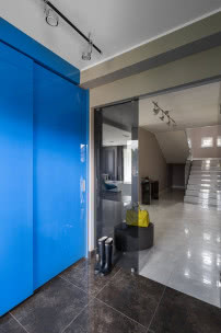 Pojemna wnękowa szafa w holu ma przesuwane drzwi w mocnym niebieskim kolorze.