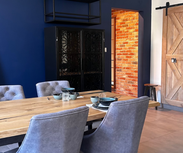 czerwona cegła na ścianie, regał w stylu loftowym, drewniane drzwi przesuwne, duży drewniany stół z krzesłami, zastawa stołowa, stołek