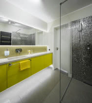 Lśniące żółte fronty szafek z MDF-u to w biało-szarym wnętrzu łazienki