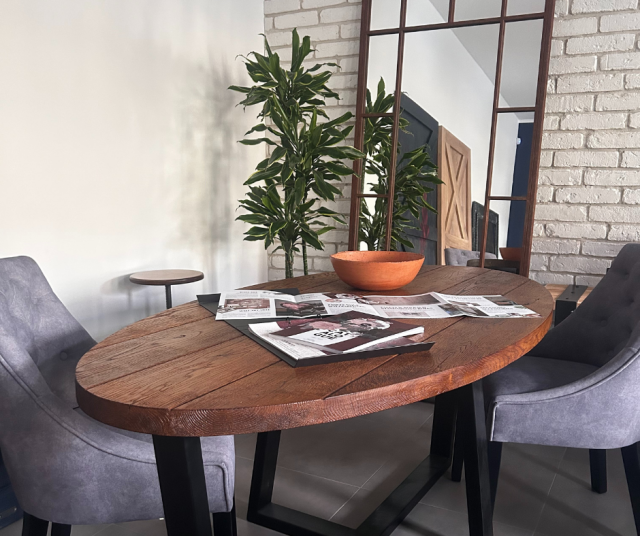 lustro, owalny stół z fotelami, stolik, duży zielony kwiat w doniczce, biała cegła na ścianie