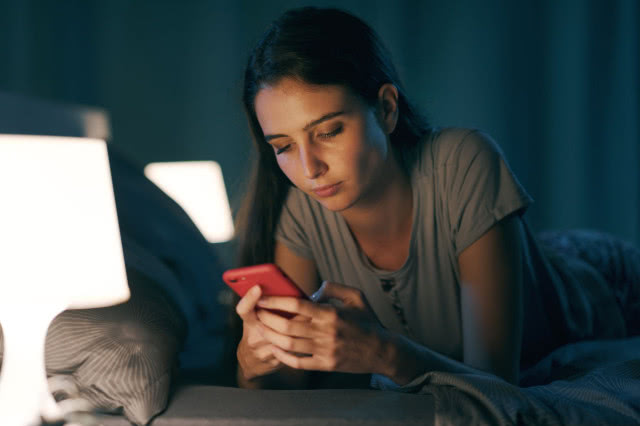 Pani trzymająca w rękach telefon, sypialnia, oświetlenie na stolikach nocnych