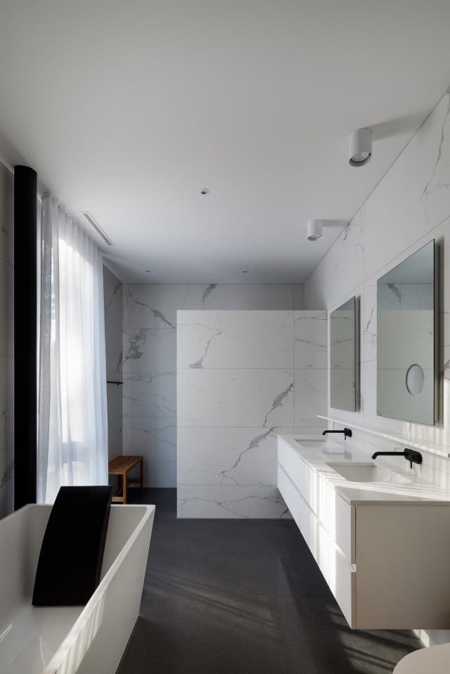 Biała łazienka z pięknym marmurem na ścianach i ciemnoszarymi wielkoformatowymi płytkami na podłodze.