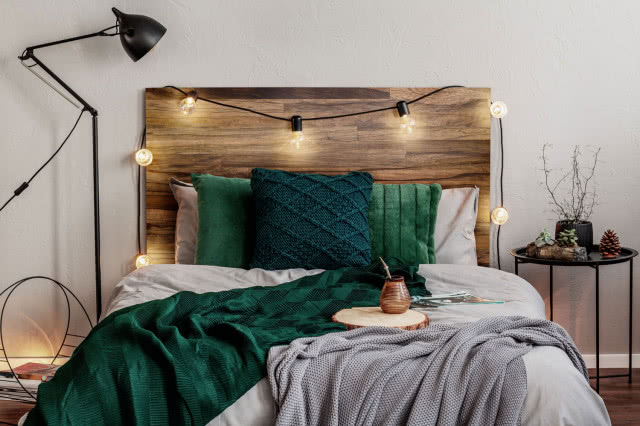 drewniany zagłówek, duże łóżko, stolik nocny, lampa podłogowa, poduszki ozdobne