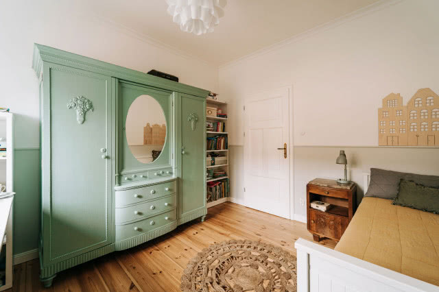 zielony kredens z dekoracyjnymi zdobieniami, okrągły dywanik, duże łóżko, drewniana podłoga