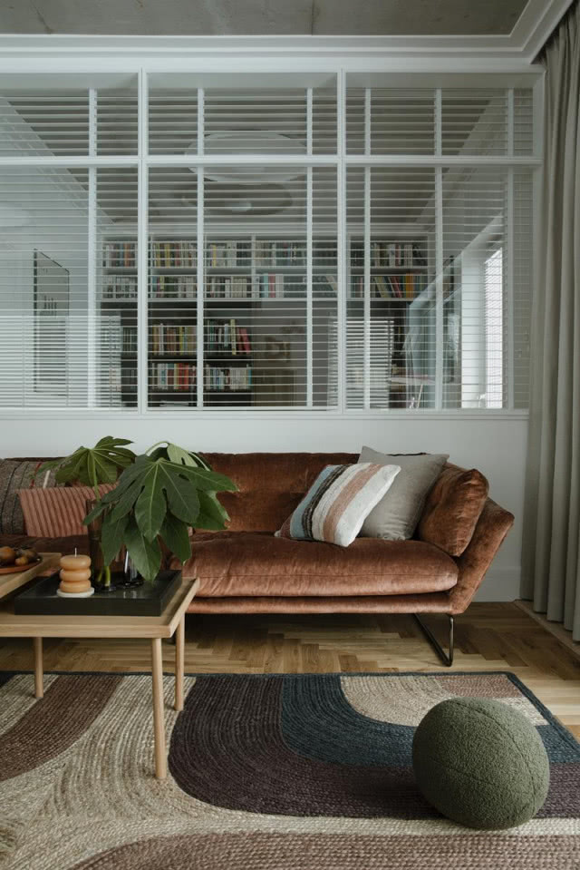 Welurowa sofa w salonie, a za nią pokój z oknem