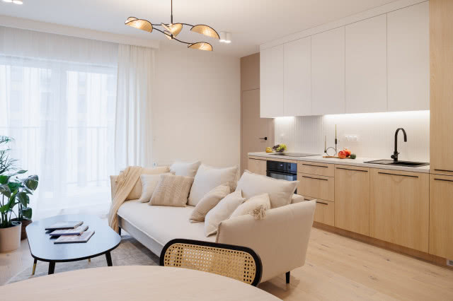 beżowa kanapa w salonie i krzesła z plecionki wiedeńskiej, w tle drewniana kuchnia