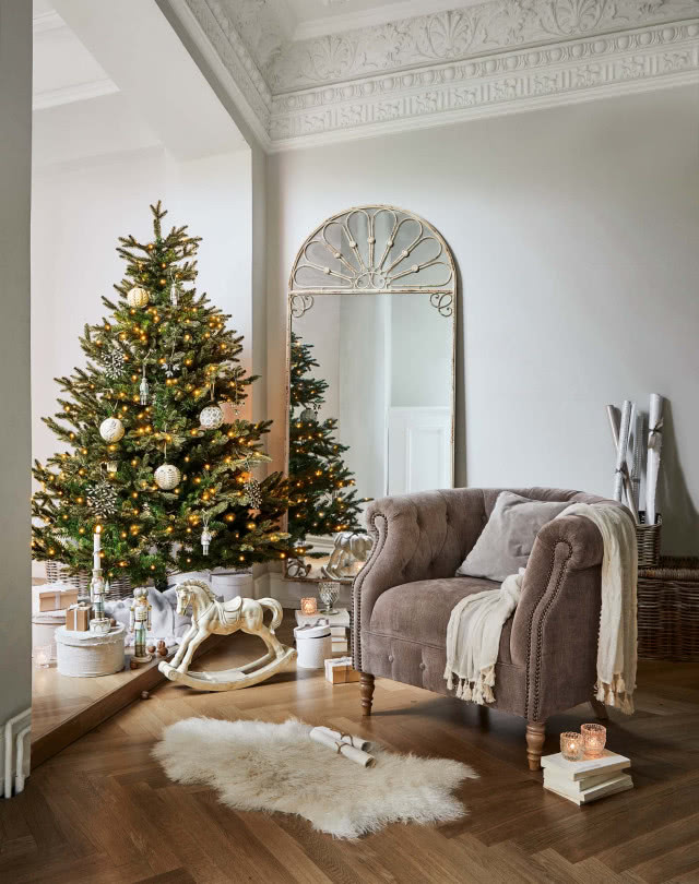 fotel, na podłodze drewniana jodełka, duże lustro, choinka, konik na biegunach, prezenty