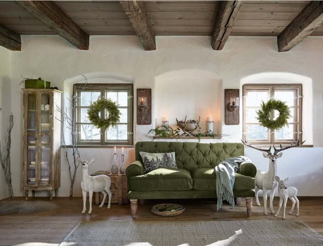 zielona kanapa, sarny, jelenie, drewniane belki na suficie, regały przeszklone, wieńce bożonarodzeniowe, dywan, komoda