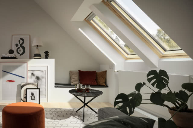 dwa okna dachowe, stolik kawowy, kawa w szklankach, puf, kanapa, kwiat w doniczce, poduszki ozdobne, lampa biurkowa, obrazy