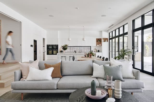 Salon w stylu skandynawskim z szarą sofą i dużymi oknami