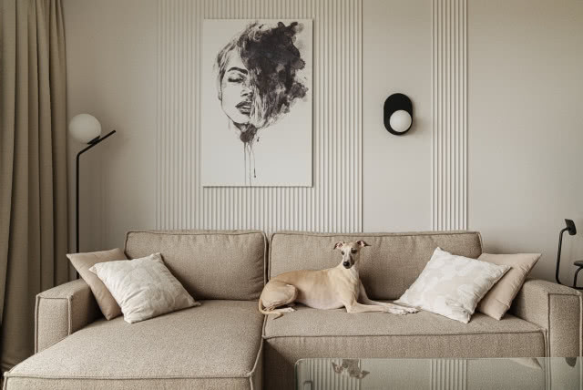 Beżowa sofa na tle kremowej ściany w salonie