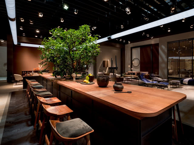 duży stół przypominający wyspę kuchenną, dużo drewnianych krzeseł, oświetlenie nad stołem, fotele, kominek, kanapy