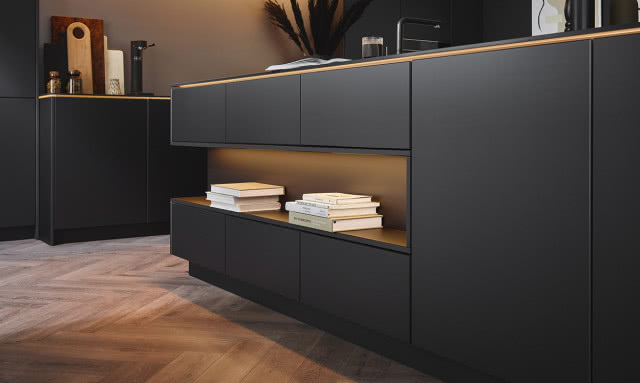 czarne, matowe fronty kuchenne, wyspa kuchenna z czarnym blatem, czarna płyta indukcyjna, czarny zlew, czarna bateria zlewozmywakowa, ekspres do kawy, wazon, misa na owoce, książka kucharska, stołek, piekarnik, przyprawy, drewniane deski do krojenia, moździerz 