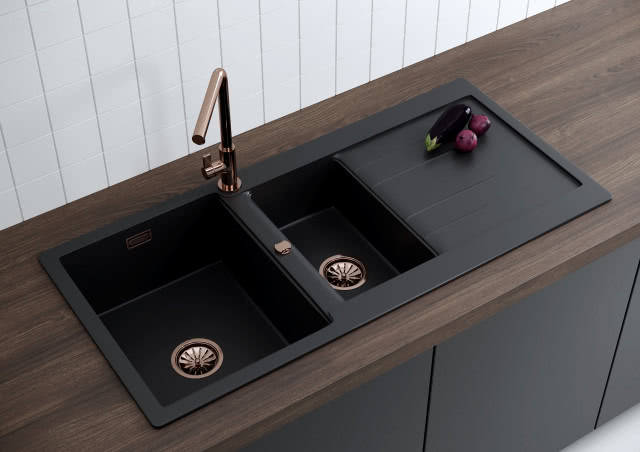 czarny zlew kuchenny, bateria i sitka odpływowe w kolorze złotym, drewniany blat kuchenny, czarne fronty kuchenne, białe płytki na ścianie